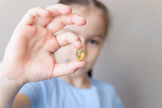 Barn håller upp en omega-3 kapsel för att illustrera kosttillskottets fördelar.