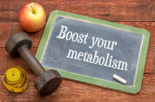 Chalkboard with 'Boost your metabolism' text, apple, dumbbell, and measuring tape on wooden background.