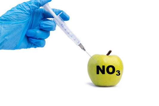 A hand in a blue glove injecting a green apple with a syringe labeled NO3, symbolizing nitrates.