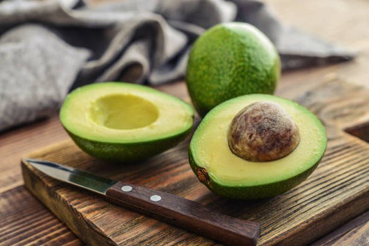 Avocado halves on a wooden cutting board with a knife, showcasing their rich green flesh and stone.