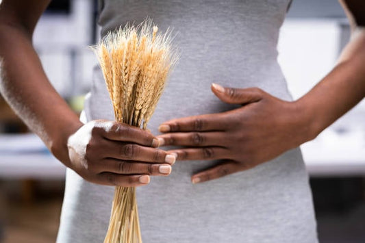 Person holding wheat stalks while touching their stomach, symbolizing gluten sensitivity issues.