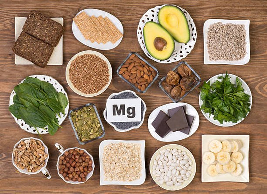 Various magnesium-rich foods including nuts, seeds, greens, and dark chocolate on a wooden table.