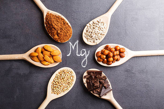 Variation of magnesium-rich foods in wooden spoons, showcasing nuts, seeds, and cacao.