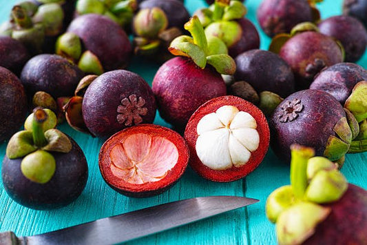 Fresh mangosteen fruits on a blue wooden surface, showcasing the vibrant outer skin and juicy white interior.