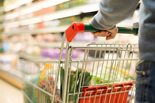 Person holding a shopping cart filled with groceries in a supermarket aisle.
