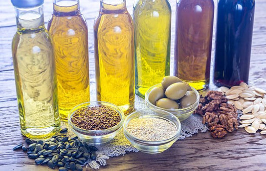 Various healthy oils and seeds, including olive oil, flaxseed oil, and nuts, displayed on a wooden table.