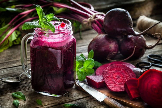 Fresh beetroot juice in a mason jar with mint, surrounded by beetroots and sliced beets on a wooden table.