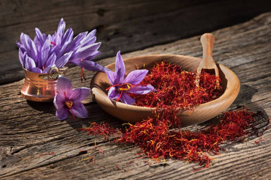 Bowl of saffron threads surrounded by purple saffron flowers on a wooden surface.