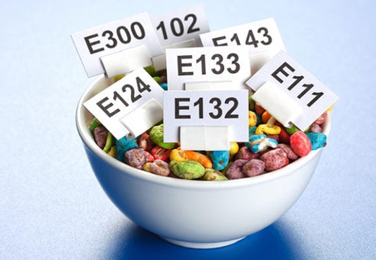 En skål med färgglad godis och skyltar med olika E-nummer tillsatser.