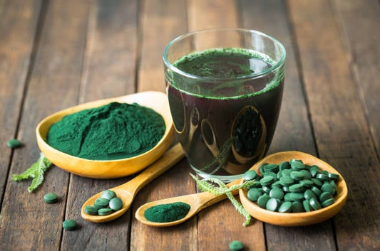 Grön smoothie med klorofyllpulver i en glas och spirulina tabletter på träbord.