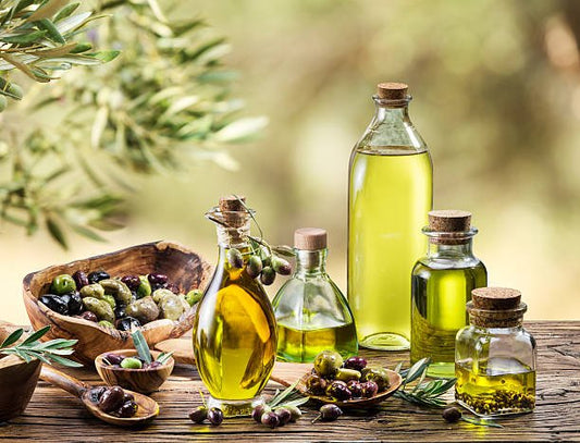Olive oil bottles and olives on a wooden table with an olive branch background, showcasing extra virgin olive oil.