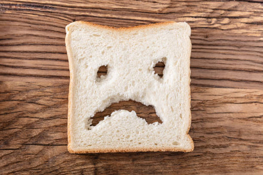 A slice of bread with a sad face carved into it, symbolizing gluten intolerance.
