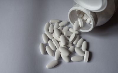 White calcium supplement tablets spilling from a bottle on a light background.