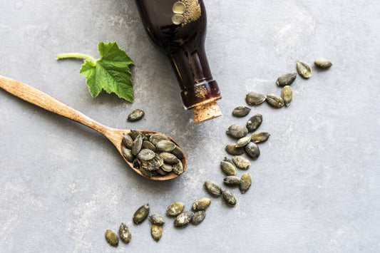 Pumpafröolja i en flaska med pumpafrön och ett träskedar, dekorerat med pumpa blad.