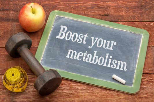 Chalkboard with 'Boost your metabolism' text, apple, dumbbell, and measuring tape on wooden background.