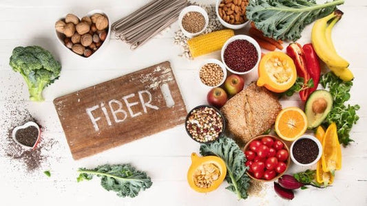 A variety of fiber-rich foods including fruits, vegetables, and grains arranged around a wooden sign labeled 'FIBER'.