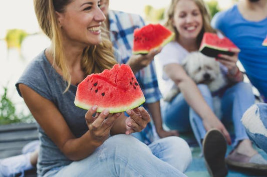 Group of friends enjoying watermelon slices by the water on a sunny day.