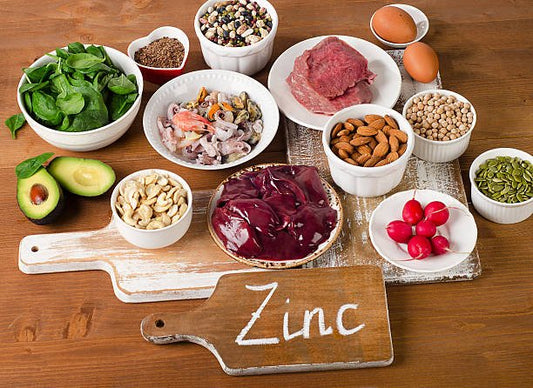 Various foods rich in zinc, including spinach, meat, nuts, and eggs, arranged on a wooden table.