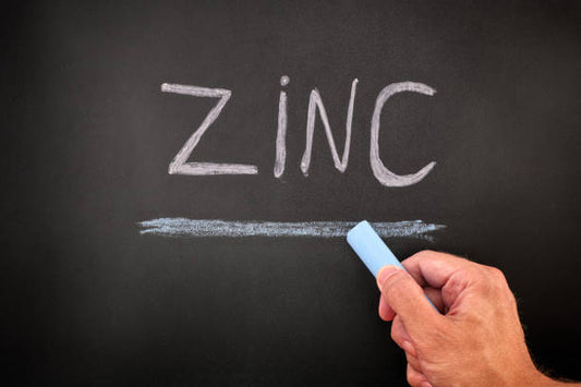 Hand writing 'ZINC' on a black chalkboard with chalk.