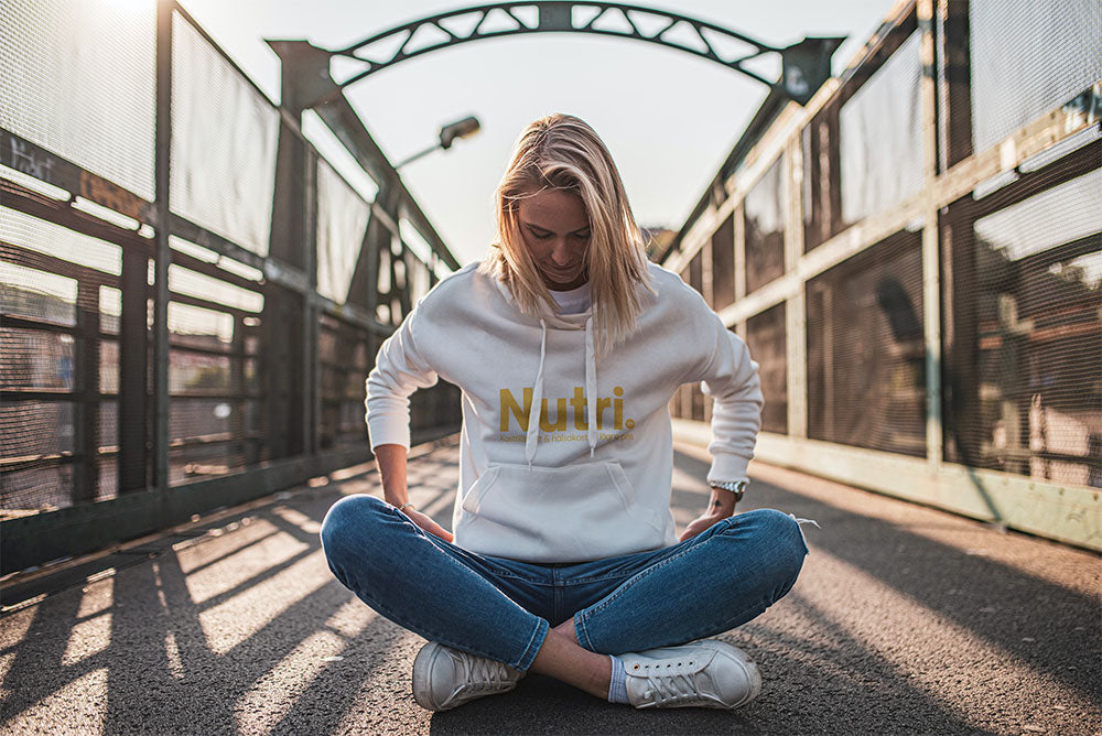 A young woman sitting cross-legged on a bridge, wearing a white hoodie with 'Nutri.' written on it.
