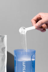 Hand pouring BCAA powder into blue shaker from Nutriversum, showcasing the mixing process.