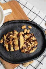 Nutriversum cookies with chocolate drizzle and nuts on a black plate, perfect healthy snack option.