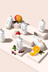 Nutriversum Liquid Collagen bottles displayed with fresh fruits like mango, strawberries, and oranges on a modern pedestal.