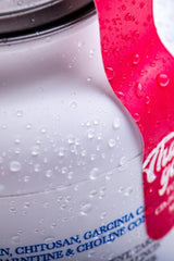 Close-up of a sleek white supplement container with water droplets and a vibrant pink label.