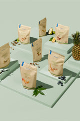 Display of Nutriversum Vegan Pro protein powder bags with fruits and seeds on a light green background.