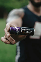 OstroVit Fat Burner Extreme Shot in a person's hand, featuring orange flavor and outdoor background.