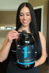 Woman holding Rule1 R1 Whey Blend protein powder, promoting its benefits and great taste.
