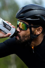 Athlete drinking from a Science in Sport water bottle while cycling, wearing a helmet and sunglasses.