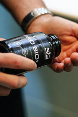 Hands holding a bottle of Science in Sport Pro Bio+ capsules, showcasing the product label and packaging.