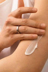 Person applying creamy vegan body lotion to dry skin on arm for hydration and softness.