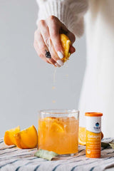Person squeezing fresh peach over a glass of peach mango collagen drink with Trace Minerals tablet.