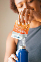 A person pouring Trace Minerals Hydration I.V. electrolyte powder from a packet into a blue water bottle.