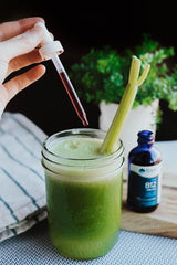 Hand holding a dropper over a green smoothie with celery and Trace Minerals B12 bottle nearby.