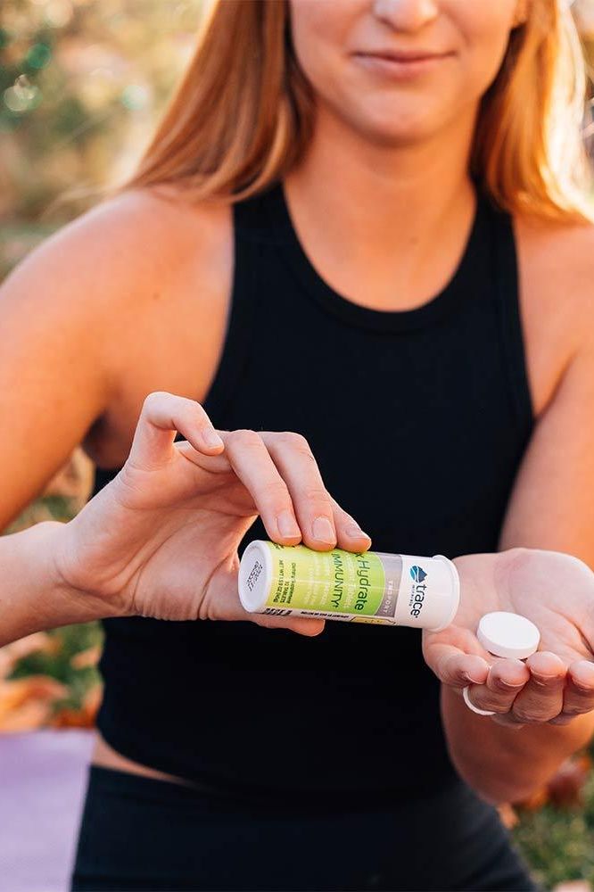 Woman holding Trace Minerals Max-Hydrate Immunity effervescent tablet bottle outdoors. Woman holding Trace Minerals Max-Hydrate Immunity effervescent tablet bottle outdoors.