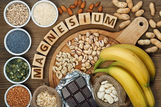 Olika livsmedel rika på magnesium, inklusive nötter, frön, bananer och choklad, på en träskärbräda.