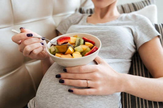 Gravid kvinna äter en skål med färska frukter, som är viktiga för hälsosam kost under graviditeten.