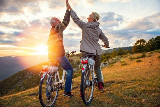 Elderly couple giving a high five while biking outdoors at sunset, celebrating an active lifestyle.