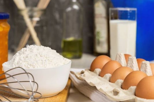 Skål med mjöl, ägg i kartong och mjölkflaska på köksbänk, ingredienser för bakning.