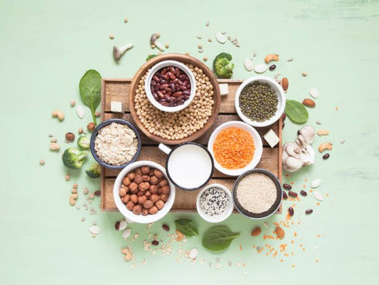 Assorted healthy beans, legumes, and grains in bowls on a wooden tray with greens and seeds.