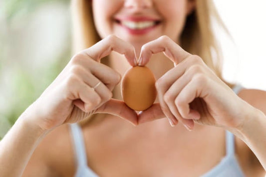 Kvinna formar ett hjärta med händerna runt ett ägg, symboliserar kärleken till äggprotein.