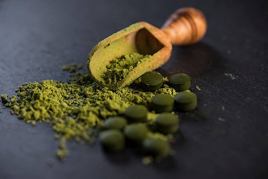 Grön spirulina-pulver och tabletter på en mörk yta med en träskopa.