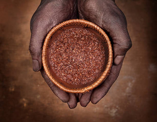 A pair of hands holding a small woven bowl filled with Amalaki Churna, highlighting its earthy texture.