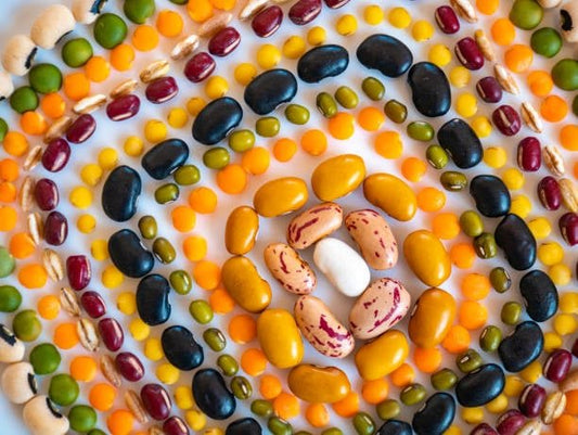 Colorful arrangement of various beans and lentils forming a spiral pattern on a white background.