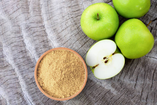 Bowl of apple pectin powder next to fresh green apples on wooden surface.