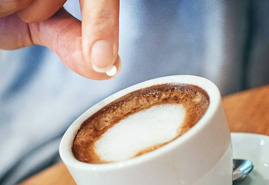 Person som tillsätter en sockerersättning i en kopp kaffe.