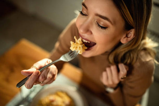 Woman enjoying a meal at a dining table, holding a fork with pasta in a warm, inviting setting.